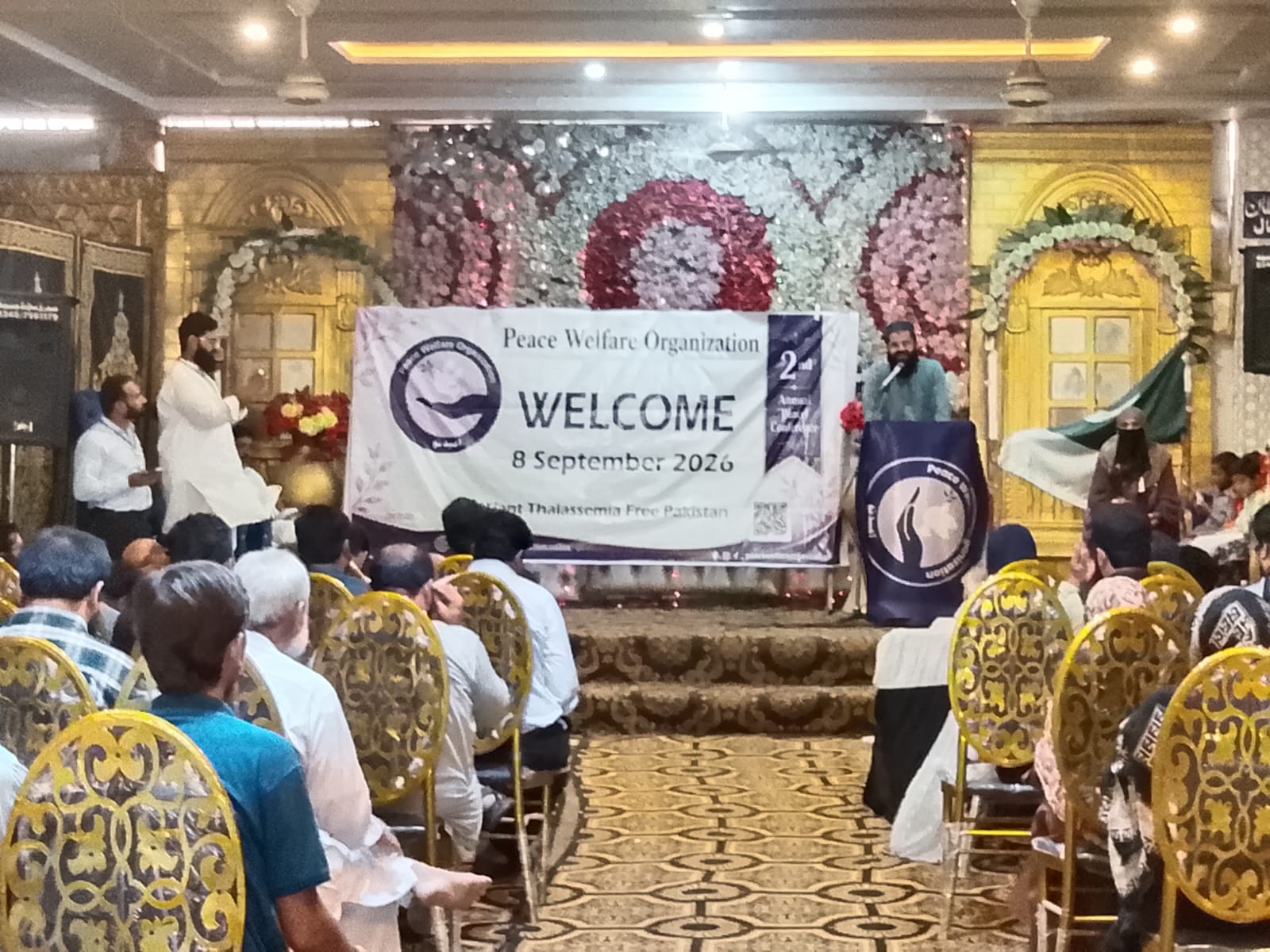 A speaker addresses the audience from the stage under the Welcome banner of 8 September 2026.